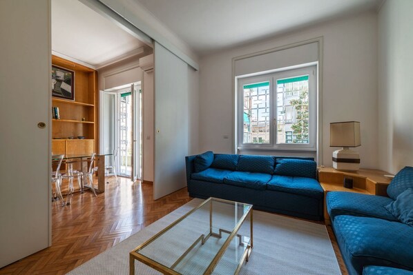 A living room with a blue sofa, a glass coffee table, and a wooden bookshelf.