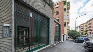 A building with a green metal gate, a brick facade, and a parking area with cars.