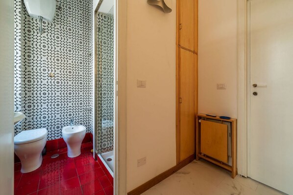 A bathroom with a toilet, bidet, and a small cabinet.