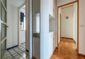 Un couloir avec un sol carrelé, des armoires blanches et un plancher en bois sur le côté droit.