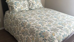 Een bed met een bloemenprint deken en bijpassende kussens, een donker houten hoofdbord en een houten vloer.