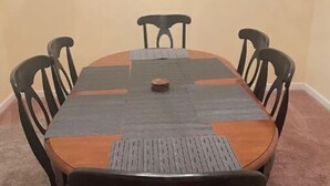 Een rechthoekige eettafel met een donkere houtkleur, omringd door zes zwarte stoelen met een klassiek ontwerp. De tafel is gedekt met een placemat en een klein decoratief object in het midden.