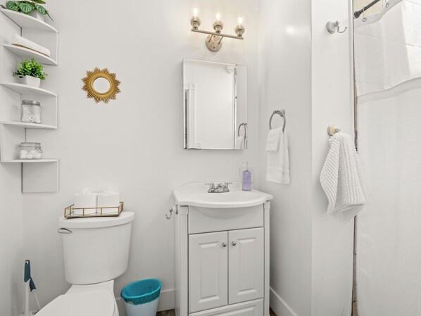 A bathroom with a toilet, sink, and shower. There are shelves with plants and a mirror above the sink.