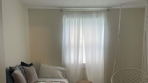 Quarto com cama, cadeira suspensa, tapete estampado e cortinas leves.