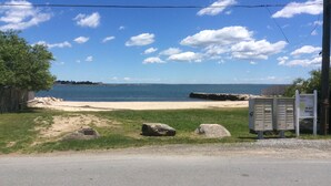 Uma praia com um muro de pedra, uma área gramada e uma estrada ao primeiro plano.