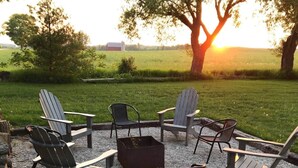En utomhusplats med sittmöbler, inklusive Adirondack-stolar, och en eldstad.