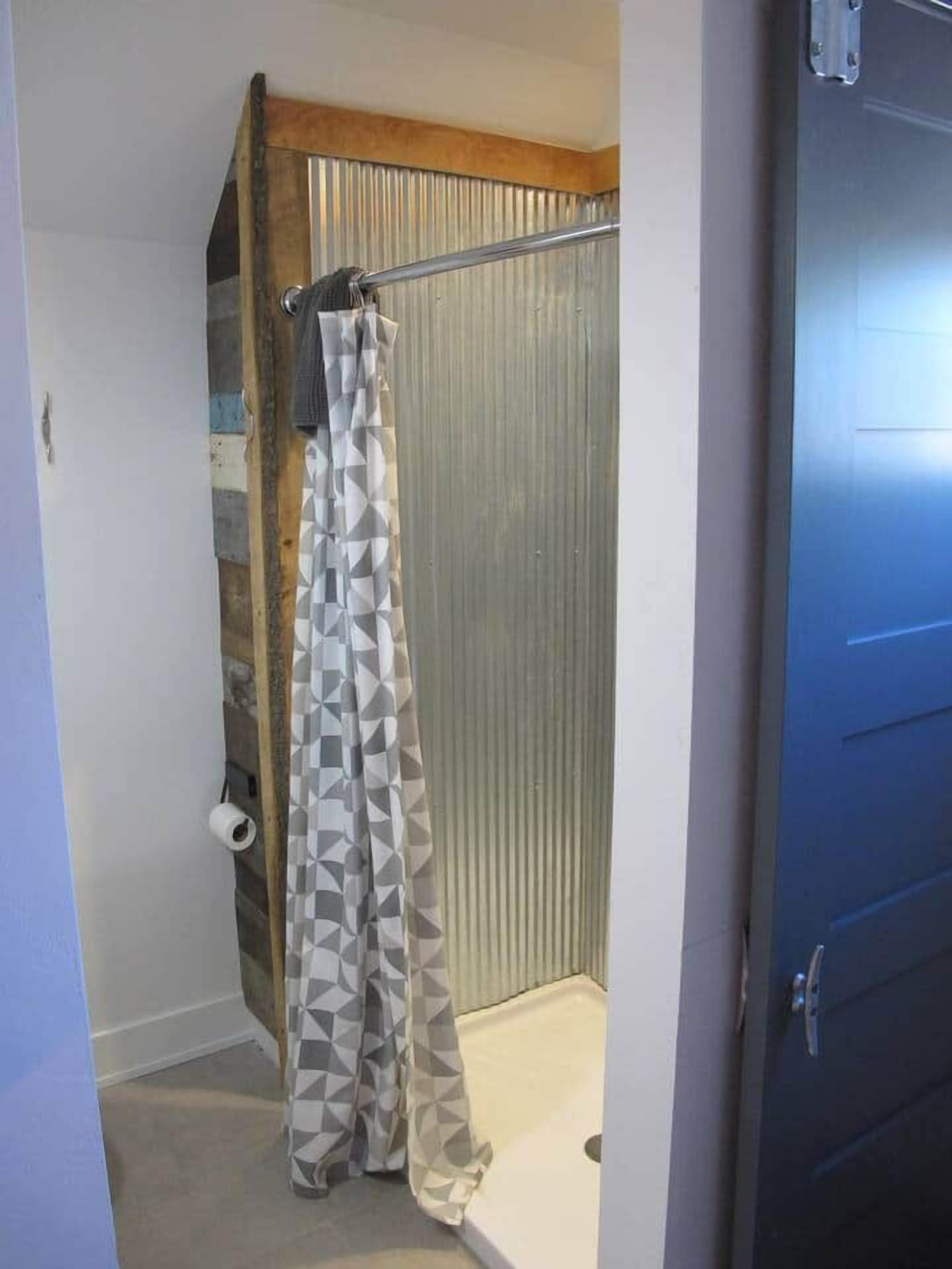 Un área de ducha con cortina de baño de estampado geométrico, un perchero y un dispensador de papel higiénico.