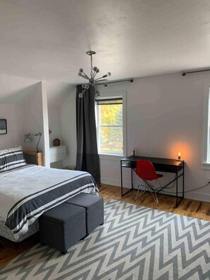 Une chambre à coucher avec un lit, un bureau, une chaise, une fenêtre et un lustre.