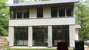 Une maison à deux étages avec de grandes fenêtres et un foyer extérieur dans le jardin.