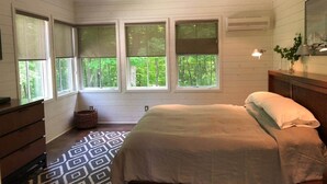 Une chambre à coucher avec un lit, une commode et des fenêtres donnant sur un espace verdoyant.