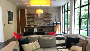 Un salon moderne avec un canapé, des fauteuils rouges et une cuisine en arrière-plan.