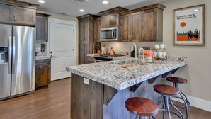 Eine moderne Küche mit Holzausstattung, Edelstahlgeräten, Granit Arbeitsplatten und einer Bar mit Hockern.