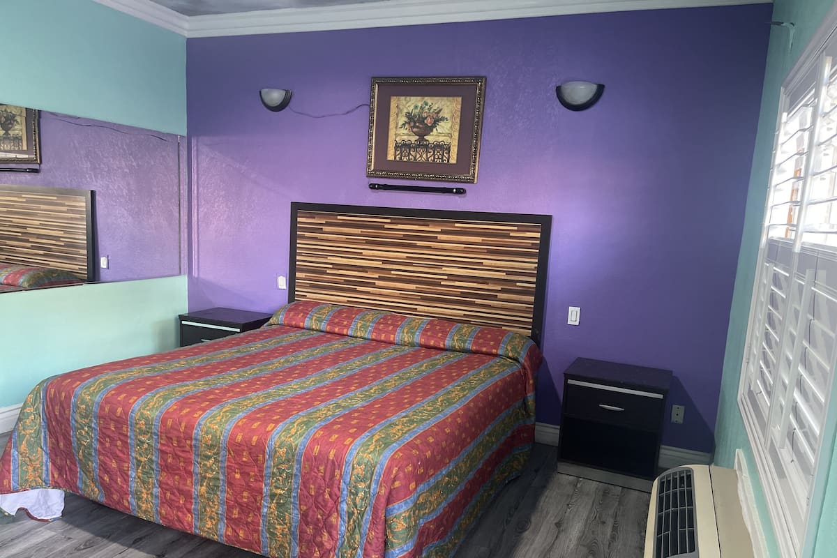 A bedroom with a bed, a nightstand, a dresser, a wall-mounted picture, and a window with blinds.