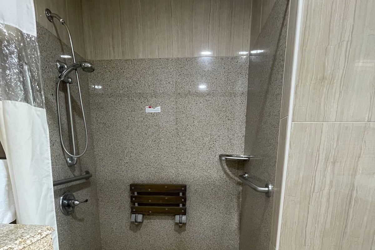 A shower stall with a glass door, a handheld showerhead, a wall-mounted faucet, a towel rack, and a bench.