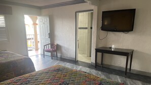 Quarto de hotel com duas camas, uma televisão na parede e uma porta para uma varanda.