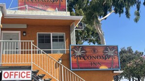 Um motel chamado 'Economy Inn' com decorações de palmeiras, uma placa de escritório e um céu azul claro ao fundo.