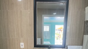 Um banheiro com bancada de granito, pia, espelho com moldura decorativa, porta-toalhas e lixeira.