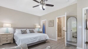 Ein Schlafzimmer mit einem Bett, Nachttischen, einem Sessel, einem Deckenventilator und einer Tür zu einem Badezimmer.