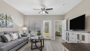 Ein Wohnzimmer mit grauem Sofa, einem Couchtisch, einem Deckenventilator und einem Fernseher auf einem Schrank.