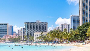 Ein Strandhotel mit mehreren Hochhäusern, Palmen und einem belebten Strand.