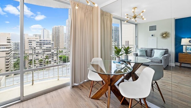 Ein modernes Wohnzimmer mit einem Glastisch, weißen Stühlen, einem grauen Sofa und Blick auf Stadtgebäude.