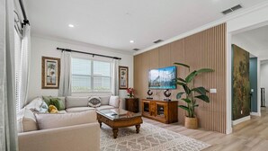 Un salon avec un canapé, une table basse, un téléviseur, un mur recouvert de panneaux en bois et une plante en pot.