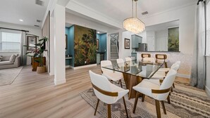 Un espace de salle à manger moderne avec une table en verre et des chaises blanches, un lustre et un grand tableau au mur.