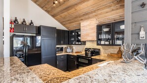 Una cocina moderna con encimeras de granito, armarios negros y techo de madera.