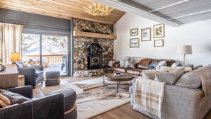 Una sala de estar acogedora con chimenea de piedra, asientos cómodos y un ventanal con vistas a una terraza nevada.