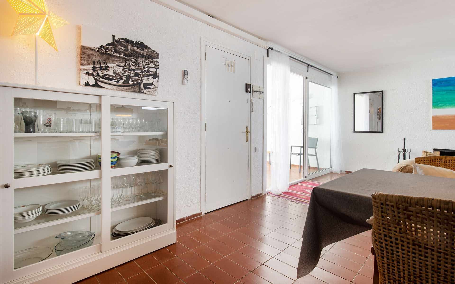 Un espace repas avec un buffet, une porte donnant sur un balcon et un fauteuil en osier.