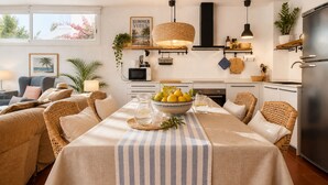 Un coin repas avec une nappe à rayures, des chaises en osier, un saladier rempli de citrons et un luminaire suspendu.