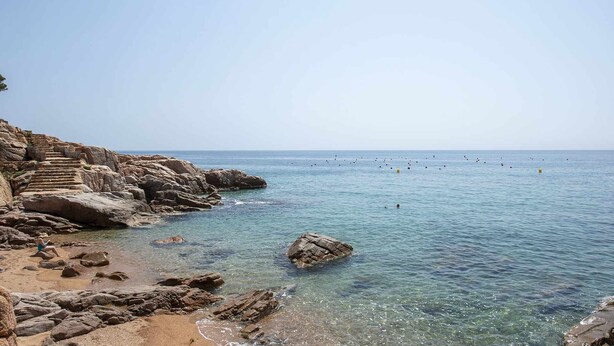 Une côte rocheuse bordée d’une eau claire, avec des marches descendant jusqu’à la plage.