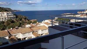 Un quartier résidentiel en bord de mer, avec des bâtiments aux toits de tuiles en terre cuite, une vue dégagée sur la mer et un balcon donnant sur le paysage.