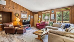 Een gezellige woonkamer met houten wanden, een leren bank, een rode fauteuil en een televisie.