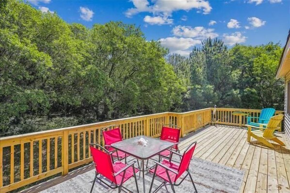 A wooden deck with a table and chairs, surrounded by trees. - Adorable 4 BR, short walk to the beach in Southern Shores! (Southern Shores)