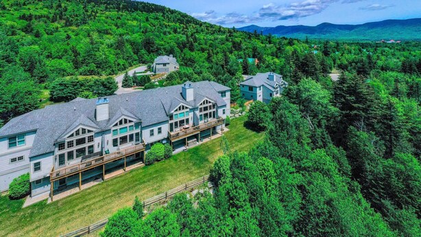 A large, multi-story house with a spacious deck and multiple rooms, surrounded by dense forest and hills. - SH3 Luxurious Stonehill Townhouse in Bretton Woods with Magnificent Views, Dog Friendly! (Bretton Woods)