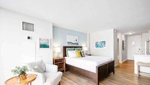 Una habitación de hotel moderna con suelo de madera, un sofá blanco, una cama de madera y obras de arte en las paredes.