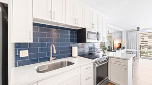 Una cocina moderna con armarios blancos, salpicadero de azulejos azules, electrodomésticos de acero inoxidable y un amplio ventanal con vistas a la ciudad.