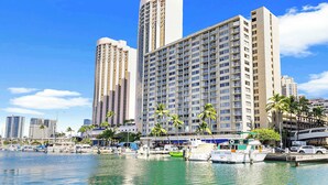 Un hotel frente al agua con varios edificios altos, un puerto deportivo con barcos y palmeras.