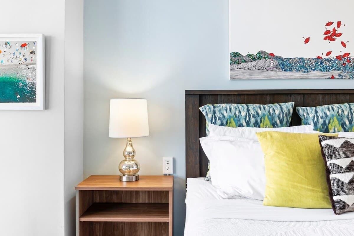 A neatly arranged hotel room with a bed, a bedside table with a lamp, and artwork on the walls.