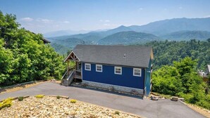 A blue cabin with a staircase leading to a porch, surrounded by a rocky landscape and mountains in the background. - What a View: Wake Up to the Wow (Gatlinburg)
