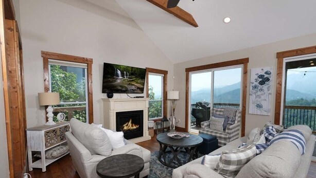 A spacious living room with a fireplace, comfortable seating, and large windows offering a view of the outdoors. - What a View: Wake Up to the Wow (Gatlinburg)