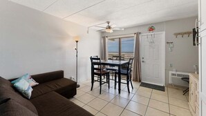 Ein Wohnbereich mit einer Couch, einem Esstisch mit Stühlen, einem Deckenventilator und Blick durch ein Fenster.