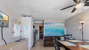 Ein Zimmer mit Esstisch, Stühlen, Deckenventilator, großem Gemälde und einer Küchenzeile.