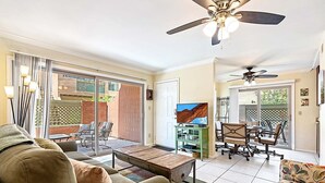 Amplia sala de estar con sofá, mesa de centro y comedor con sillas. Cuenta con una puerta corrediza de vidrio que da a un patio con mobiliario exterior.