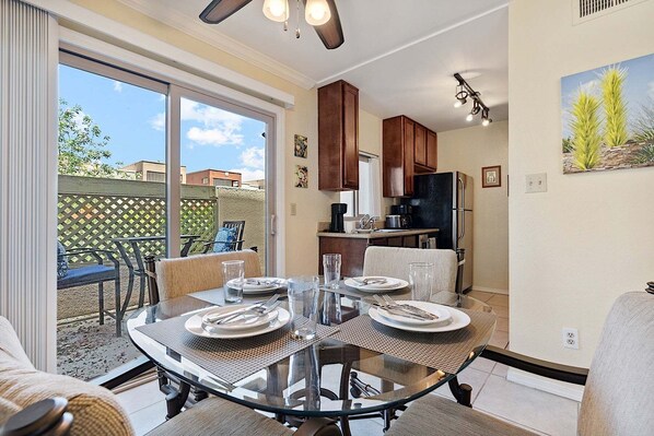 A dining area with a glass table, chairs, and a kitchen in the background.