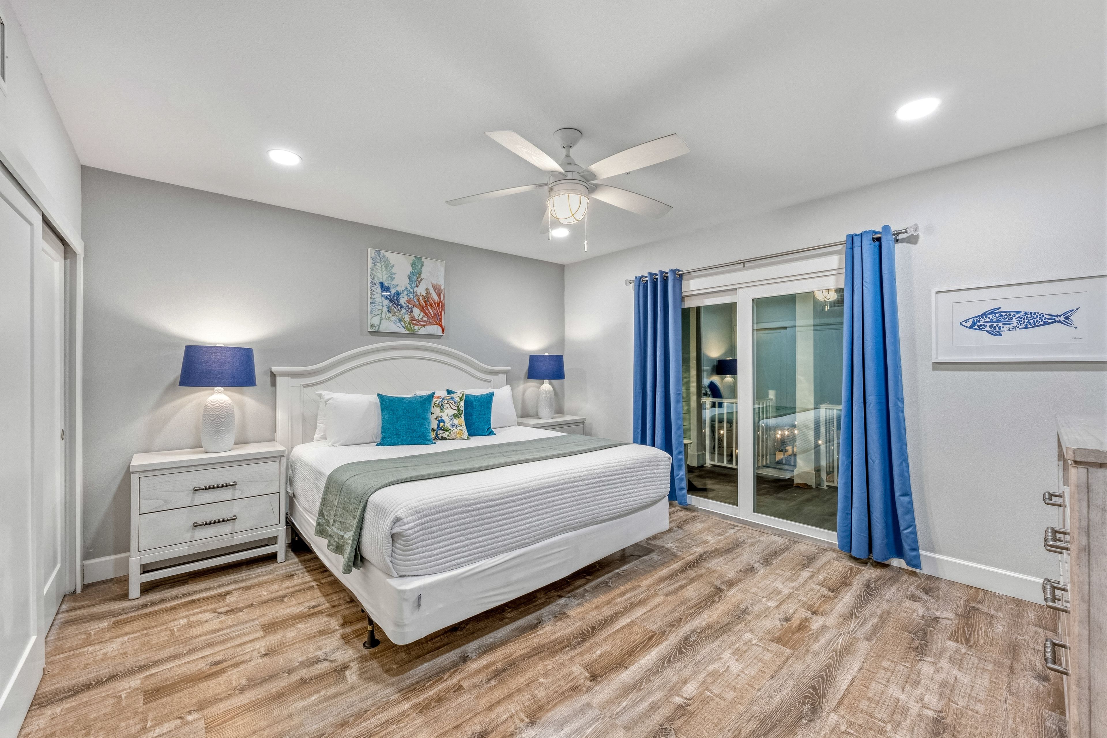 A bedroom with a bed, nightstands, a ceiling fan, and a view of the outside through a glass door.