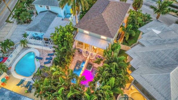 An aerial view of a residential property with a swimming pool, multiple lounge chairs, and a well-maintained garden with palm trees.
