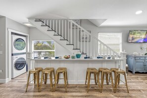 Une cuisine moderne dotée d’un îlot central, de tabourets de bar, d’un escalier et d’un lave-linge.