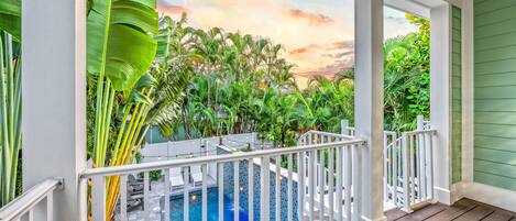 Un espace piscine offrant une vue sur la végétation tropicale et un ciel au coucher du soleil.